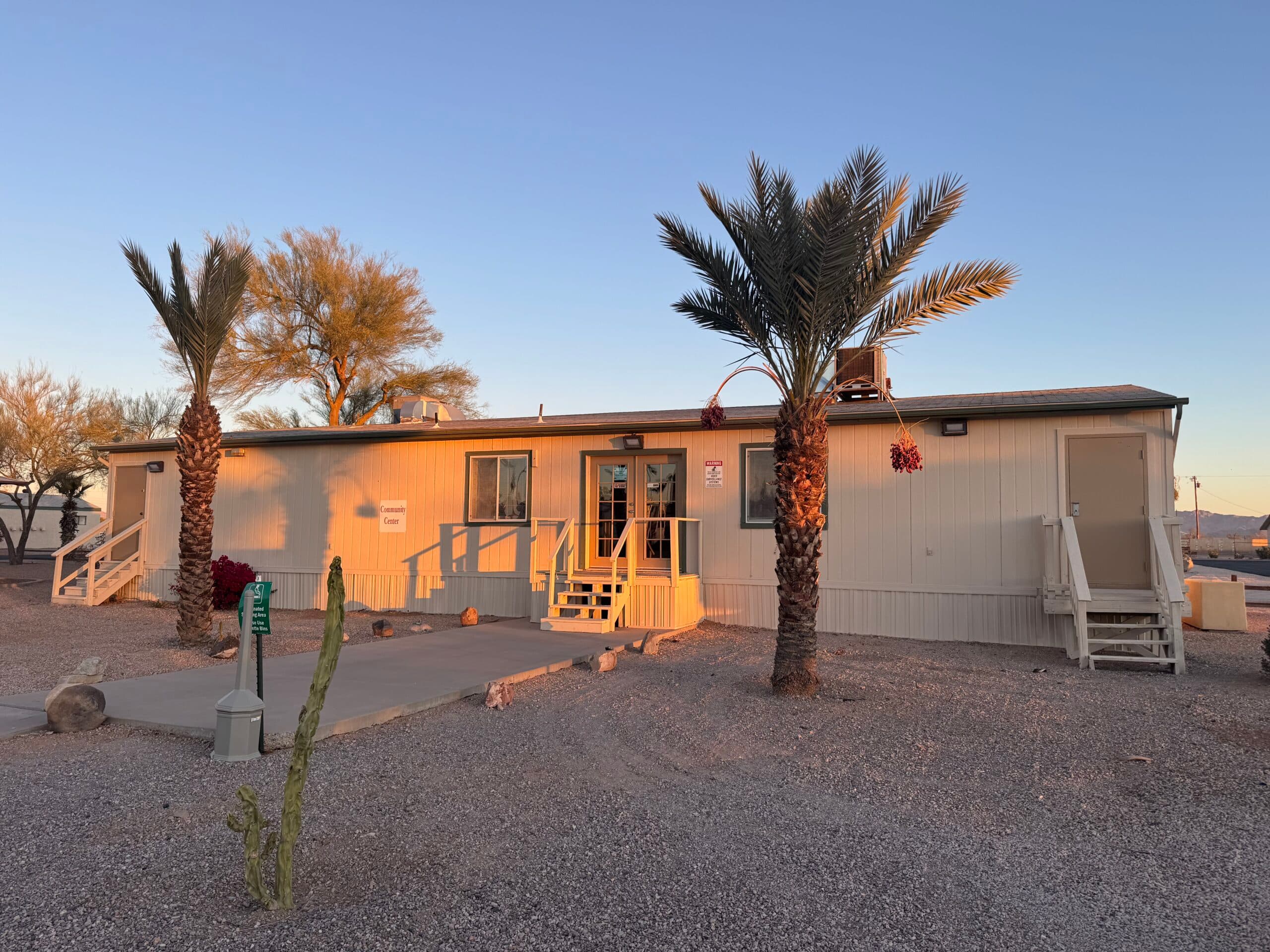 A park building with ramps to its front entry, shaded by palm trees, at Saddle Mountain RV Park.